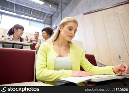 education, high school, university, learning and people concept - student girl writing to notebook at lecture hall