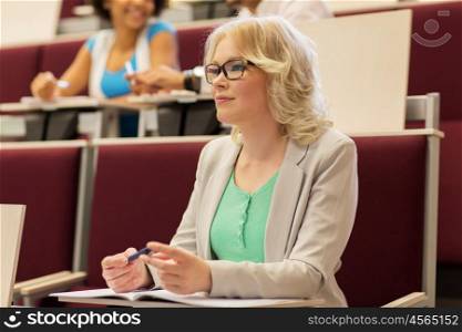 education, high school, university, learning and people concept - student girl writing to notebook in lecture hall