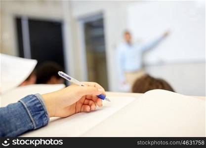 education, high school, university, learning and people concept - student hand writing to notebook at exam or lecture