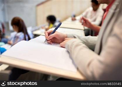 education, high school, university, learning and people concept - student writing to notebook at exam or lecture