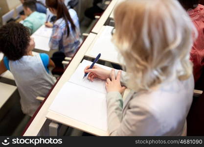 education, high school, university, learning and people concept - student writing to notebook at exam or lecture