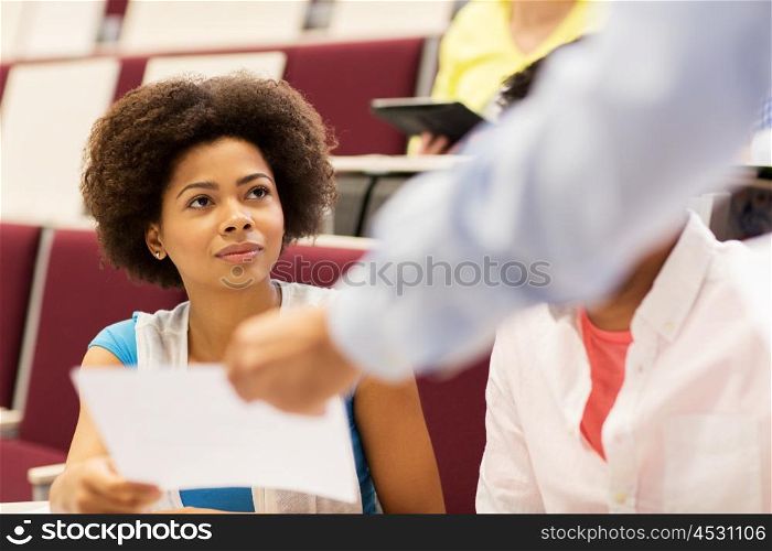 education, high school, university, learning and people concept - teacher giving test to student girl on lecture