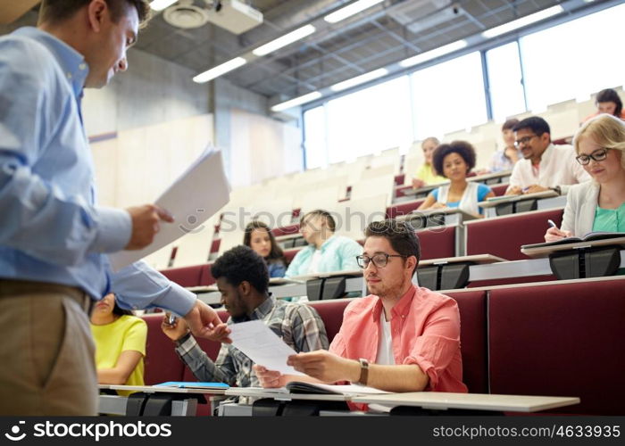 education, high school, university, learning and people concept - teacher giving tests to students at lecture