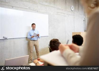 education, high school, university, teaching and people concept - group of international students and teacher with papers standing at white board at lecture