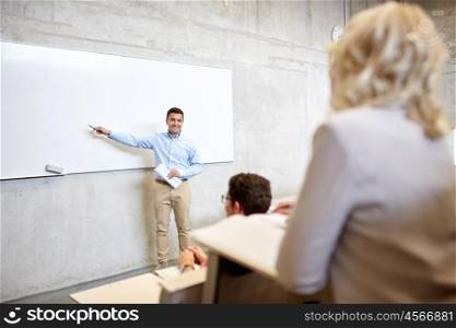 education, high school, university, teaching and people concept - group of students and teacher with marker standing at white board at lecture