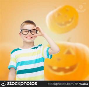 education, holidays, childhood, vision and people concept - smiling little boy in glasses over halloween pumpkins background
