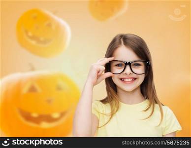education, holidays, childhood, vision and people concept - smiling little girl in glasses over halloween pumpkins background