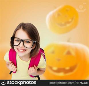 education, holidays, childhood, vision and people concept - smiling little girl in glasses over halloween pumpkins background