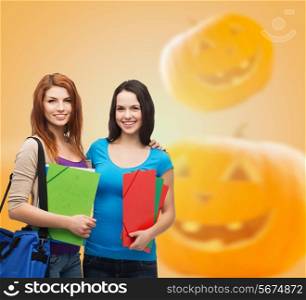 education, holidays, school, friendship and people concept - smiling student girls with books and bag over halloween pumpkins background