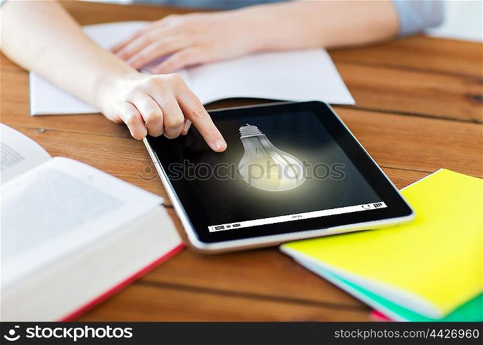 education, idea, technology and internet concept - close up of student woman with light bulb on tablet pc computer and notebook at home
