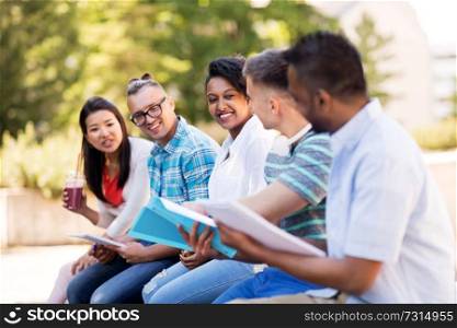 education, international and people concept - group of happy exchange students with notebook and takeaway drinks talking outdoors. students with notebook and takeaway drinks