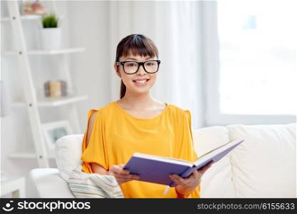 education, knowledge, leisure, literature and people concept - smiling young asian woman or student girl in glasses reading book at home