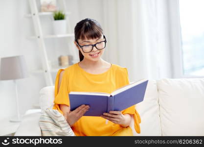 education, knowledge, leisure, literature and people concept - smiling young asian woman or student girl in glasses reading book at home