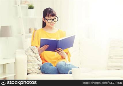 education, knowledge, leisure, literature and people concept - smiling young asian woman or student girl in glasses reading book at home. smiling young asian woman reading book at home. smiling young asian woman reading book at home
