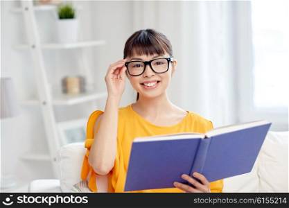 education, knowledge, vision, literature and people concept - smiling young asian woman or student girl in glasses reading book at home
