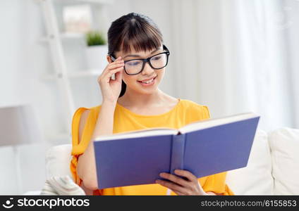 education, knowledge, vision, literature and people concept - smiling young asian woman or student girl in glasses reading book at home