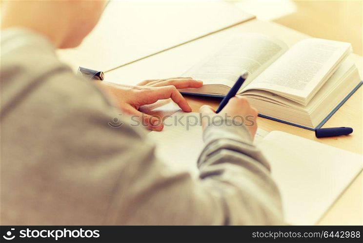 education, learning and people concept - close up of student boy with notebook and book writing school test. close up of student writing to notebook at school