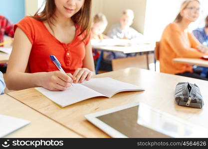 education, learning and people concept - close up of student girl with notebook and tablet pc writing school test