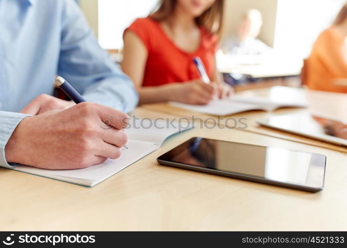 education, learning and people concept - close up of students with notebook and tablet pc computer writing school test