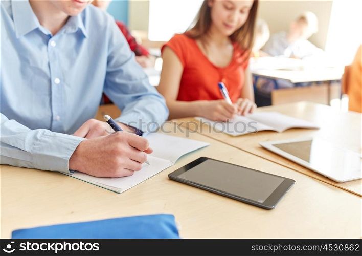 education, learning and people concept - close up of students with notebook and tablet pc computer writing school test