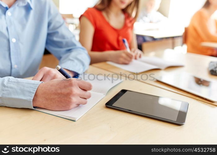 education, learning and people concept - close up of students with notebook and tablet pc computer writing school test