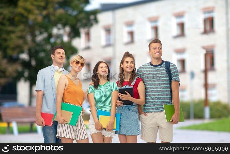 education, learning and people concept - group of smiling students with notebooks, books and folders over school or campus background. students with books and folders over school