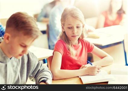 education, learning and people concept - group of students with books writing school test and girl cheating. group of students with books writing school test