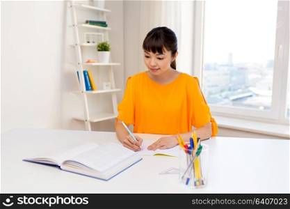 education, learning and people concept - happy asian student girl with book and notebook at home. happy student girl with book and notebook at home