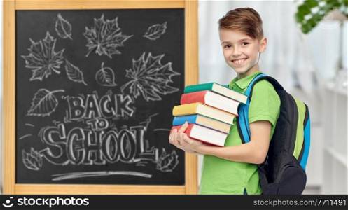 education, learning and people concept - happy smiling student boy with bag and books over chalkboard with back to school lettering on background. happy student boy with school bag and books