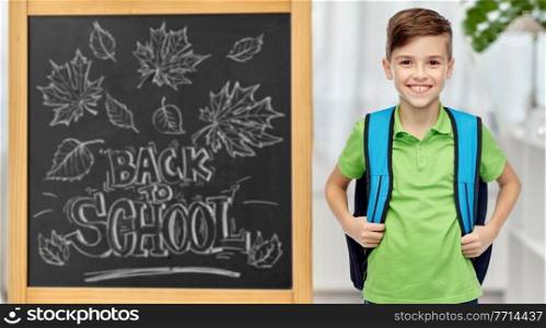 education, learning and people concept - happy smiling student boy with bag over chalkboard with back to school lettering on background. happy student boy with school bag