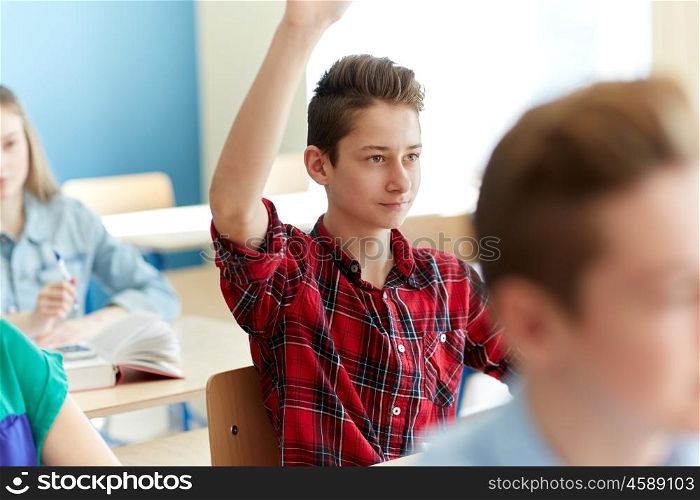 education, learning and people concept - happy student boy raising hand at school lesson