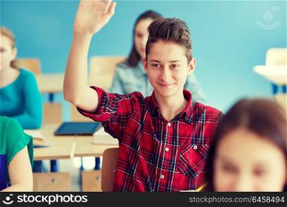 education, learning and people concept - happy student boy raising hand at school lesson. happy student boy raising hand at school lesson