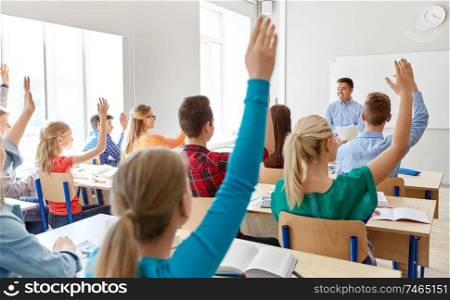 education, learning and people concept - male teacher and group of high school students raising hands in classroom. group of high school students and teacher