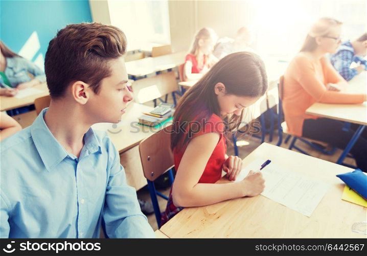 education, learning, cheating and people concept - group of students writing school test. group of students writing school test