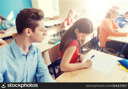 education, learning, cheating and people concept - group of students writing school test. group of students writing school test