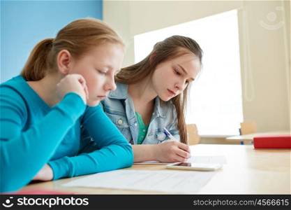 education, learning, technology and people concept - student girls with smartphone writing school test. student girls with smartphone writing school test
