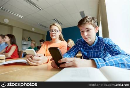 education, learning, technology, communication and people concept - students with smartphone texting at school lesson
