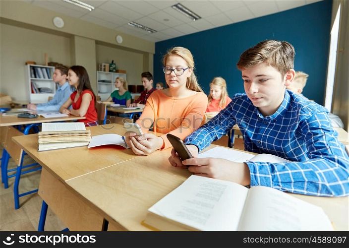 education, learning, technology, communication and people concept - students with smartphone texting at school lesson