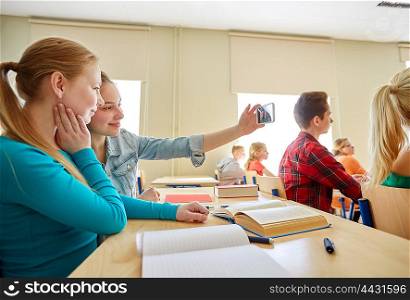 education, learning, technology, friendship and people concept - student girls with smartphone taking selfie at school lesson