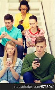 education, leisure and technology concept - busy students with smartphones sitting on staircase