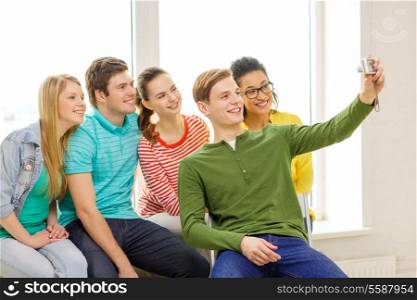 education, leisure and technology concept - five smiling students taking picture with digital camera at school