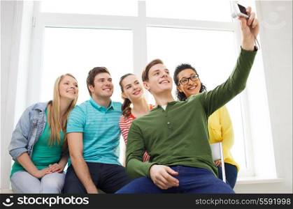 education, leisure and technology concept - five smiling students taking picture with digital camera at school