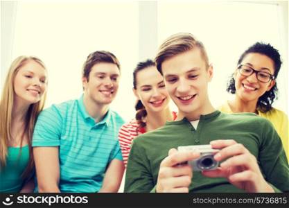 education, leisure and technology concept - five smiling students with digital camera at school