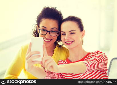 education, leisure and technology concept - two girlfriends taking selfie with smartphone camera