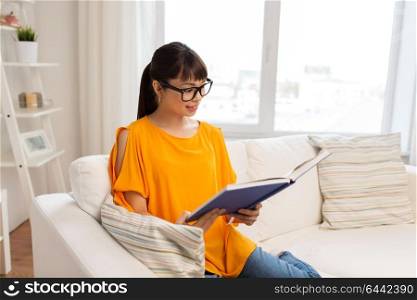 education, literature and people concept - smiling young asian woman in glasses reading book at home. young asian woman in glasses reading book at home