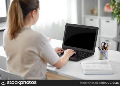 education, online school and distant learning concept - student woman with laptop computer and book typing at home. student woman with laptop and book at home