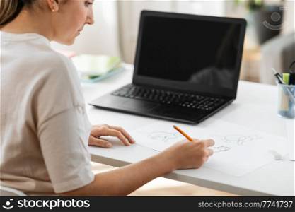 education, online school and distant learning concept - student woman with laptop computer drawing picture of cat on paper at home. student woman with laptop drawing picture at home