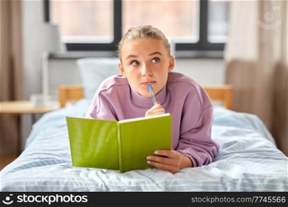 education, people and leisure concept - thinking girl with diary lying on bed at home. thinking girl with diary lying on bed at home