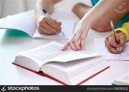 education, people and school concept - close up of students hands with textbooks writing to notebooks at school