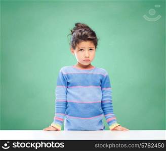 education, people, childhood and emotions concept - sad little school girl over green chalk board background